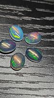 Five oval opal cabochons on black textured surface showing multicoloured fire