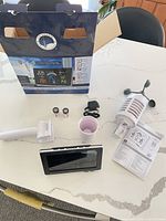 All components laid out: display, sensor, bracket, cup, two batteries, adapter, manual with outer box