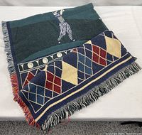 Folded golf motif woven throw showing golfer figure and argyle pattern with fringe