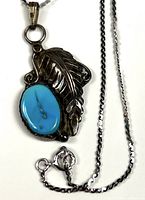 Front view of pendant on chain showing turquoise cabochon, feather design, bezel and chain