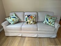 Front view of beige three-seat sofa with three throw pillows displayed