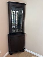 Full view of corner curio cabinet closed showing dark brown finish and glass door