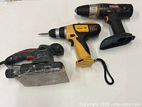 Three power tools laid out: Jobmate sander, yellow/black drill, Ryobi drill