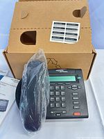 Phone base, handset in plastic, box behind, label sheet visible