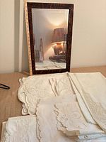 Stack of ivory/white embroidered linens alongside oak framed mirror