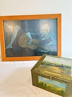 Framed Picasso print beside decorative scenic tin