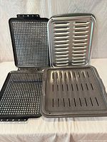 Four broiler pans and inserts displayed upright and flat to show styles and finishes