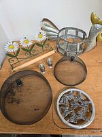 All items laid out on table: paper towel holder, two splatter screens, rooster basket, shot glasses, butterfly trivet