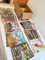 Tabletop view of multiple Outdoor Life and Guns magazines with additional stack in cardboard box