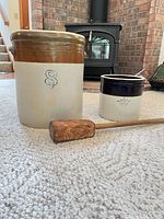 Large and small stoneware crocks with wooden mallet displayed on carpet
