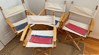 Four wood director chairs with white canvas panels, sealed red and navy replacement covers displayed on seats