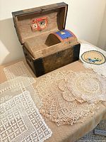 open wooden trunk with interior tray, several crocheted and embroidered linens displayed