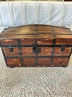 Front view of domed wood trunk showing metal straps, latches, lock plate, veneer wear
