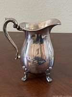 Front view of silver-tone pitcher showing ornate feet and handle