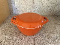 Side view of orange enameled Dutch oven with lid in place