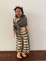 Full view of doll standing against wall showing dress and overall condition