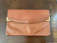 Front view of brown leather clutch showing gold-tone corner accents