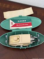overall view of buttonholer in open teal case with booklet and fabric strip
