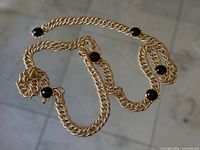 Full view of gold-tone chain belt-necklace laid out showing overall length and five black cabochon stations