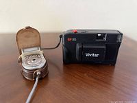 Front view of Vivitar EF35 camera beside Hanimex Sekonic exposure meter in open leather case