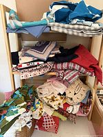Shelving unit holding multiple stacks of assorted vintage fabric pieces and basket of fabric scraps