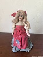 Front view of antique doll with red apron and visible fabric damage