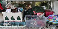 Shelf containing all Christmas décor items: light bulbs, string lights, craft box, tote of ornaments, garland, tins, dinnerware