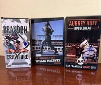 Front view of three boxed figures: Brandon Crawford bobblehead, Willie McCovey statue, Aubrey Huff bobblehead