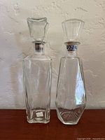 Front view of both clear glass decanters showing shapes, stoppers, and seal