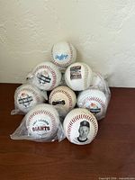 Stacked view of eleven baseballs showing Rawlings ball on top, multiple Giants commemorative designs, some in plastic