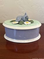 Front view of closed lavender ceramic trinket box showing kitten and floral lid