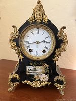 Front view of hand-painted gilded mantle clock showing dial, painted panel, and ornate gold mounts