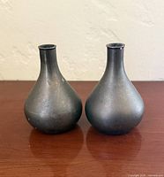 Front view of both matching metal bud vases showing shape, finish and minor wear