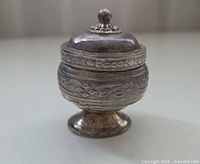 Front view of footed metal trinket box with lid