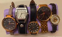 Five watches displayed on cushion showing faces and straps