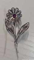 Front view of silver filigree flower brooch showing purple center stone and leaf detail