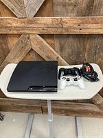 PS3 Slim with two controllers and cabling on table