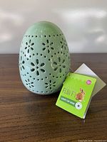 Front view of mint green ceramic egg with floral cutouts and hang tag