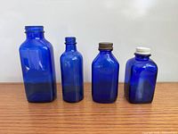 Front view of four cobalt blue bottles displaying varying heights and caps