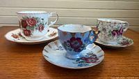Front view of three floral porcelain teacups and saucers on wooden surface