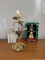 Full view of assembled gold metal angel chime carousel, four white candles and product box
