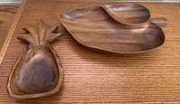 Leaf and pineapple shaped carved wooden trays side by side