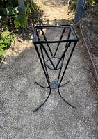 Full view of tall wrought iron plant stand on pathway