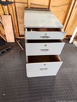 Cabinet front showing three drawers, top drawer slightly open, locks and handles visible