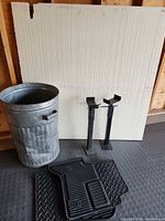 Group shot of galvanized trash can, two jack stands, three black floor mats