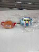 Both miniature teapots in plastic sleeves