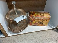 Lot overview showing boxed apple peeler beside two-tier metal serving tray