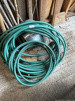 Coiled green rubber garden hose on floor showing overall condition and connectors