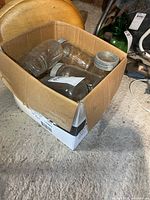 Box with multiple clear glass canning jars, some with lids