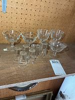 Group view of five stemmed coupes and six shot glasses on shelf